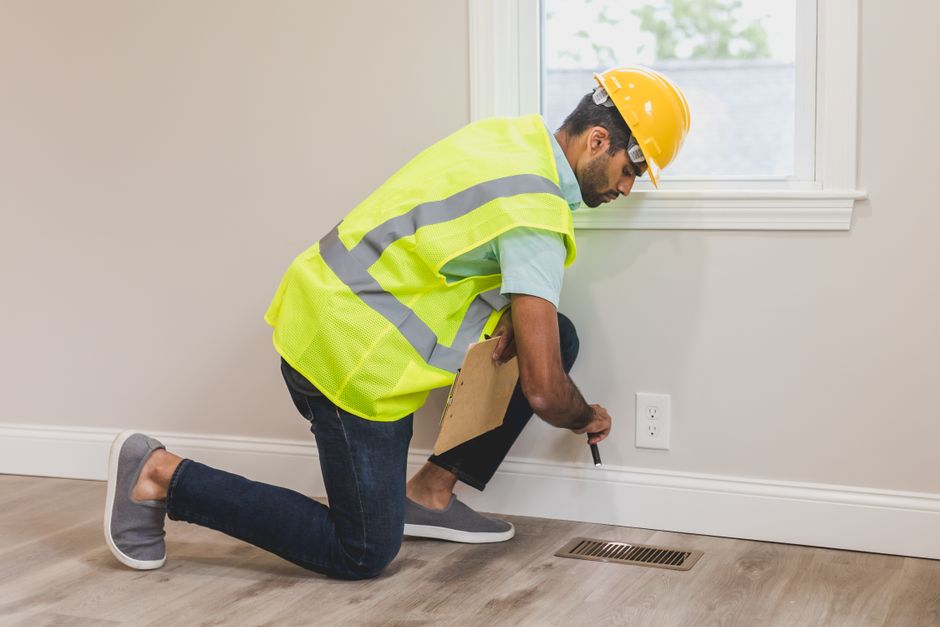 Inspector checking a baseboard and floor vent during a termite inspection